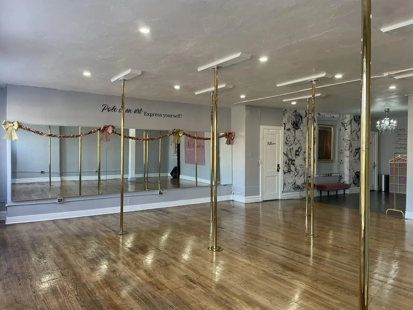 The empty studio: gold poles on a hardwood floor in front of a wall of mirrors